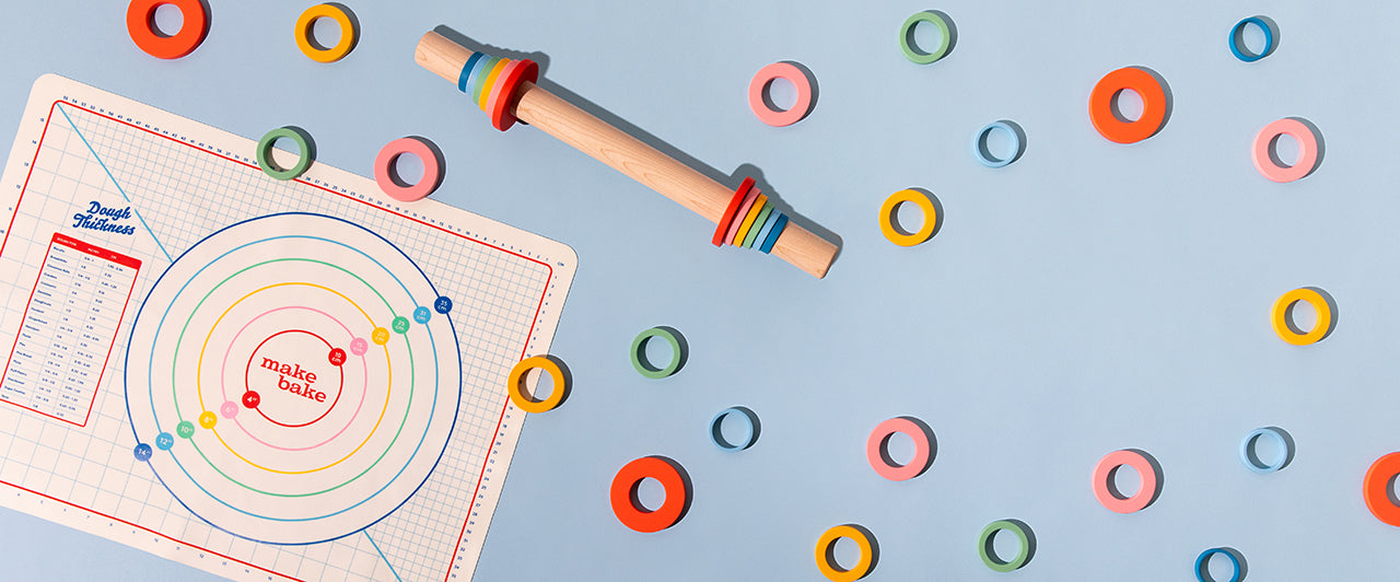 Colorful adjustable rolling pin with silicone depth rings and a matching silicone mat with pie ring measurements on a blue background
