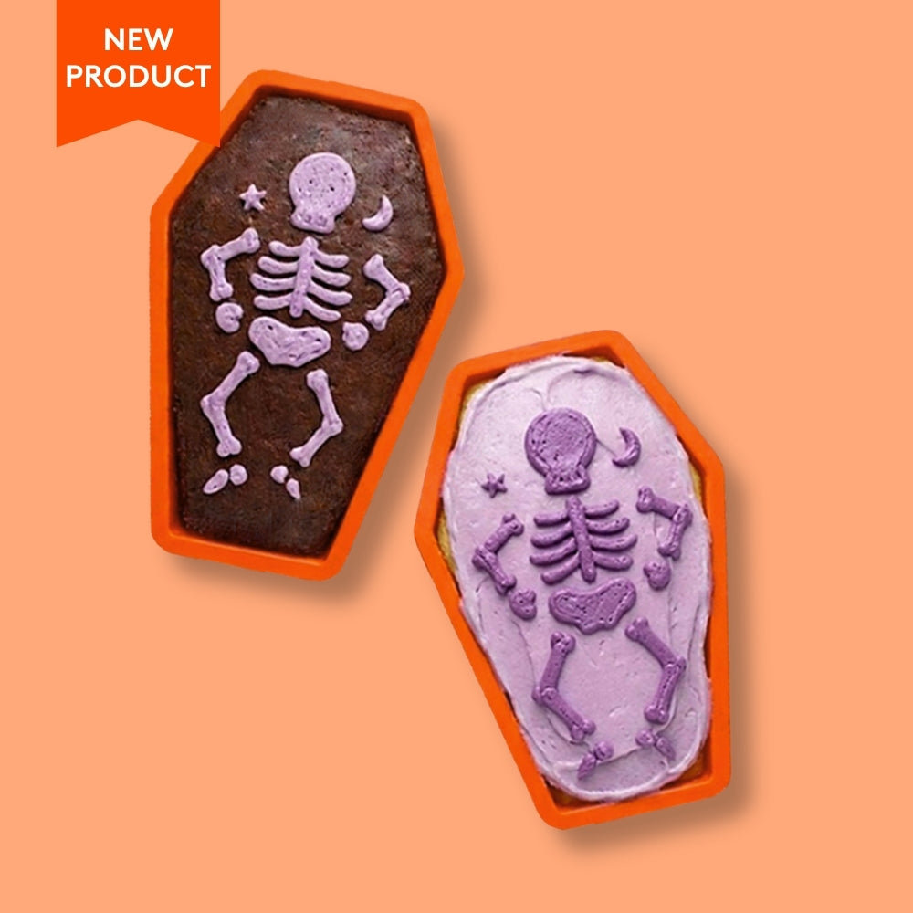 Two Halloween-themed coffin shaped chocolate cakelets with skeleton designs on an orange background.