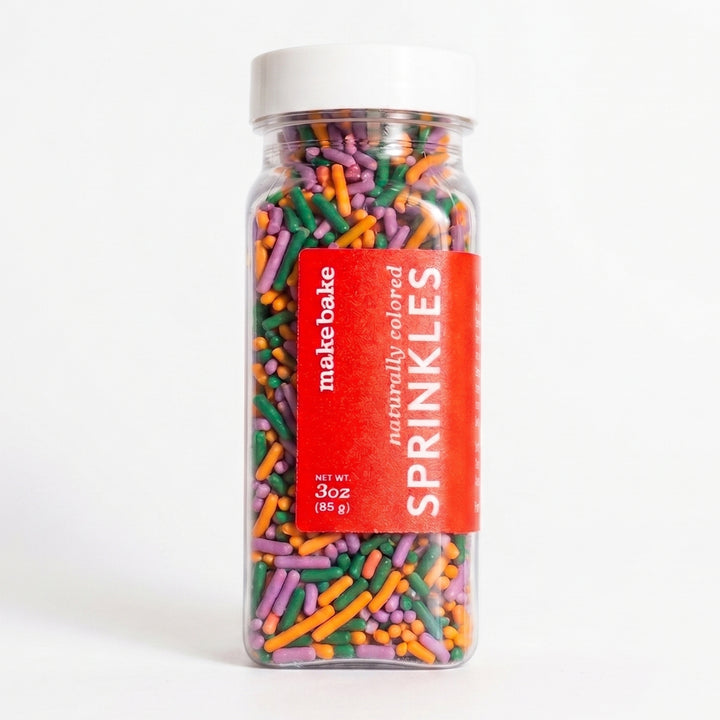 Bottle of Make Bake brand dye-free sprinkles Halloween mix includes orange, purple and green jimmies in a clear bottle with a red label.