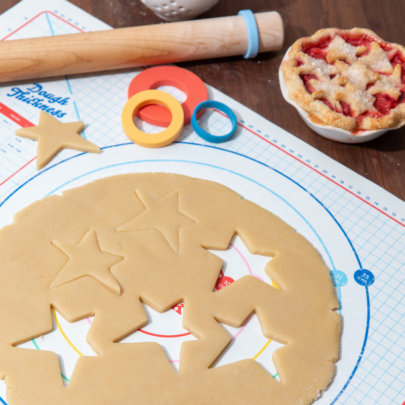 Dishwasher safe silicone baking mat shown with pie measurement rings in inches and mm with wooden rolling pin and dough thickness rings.