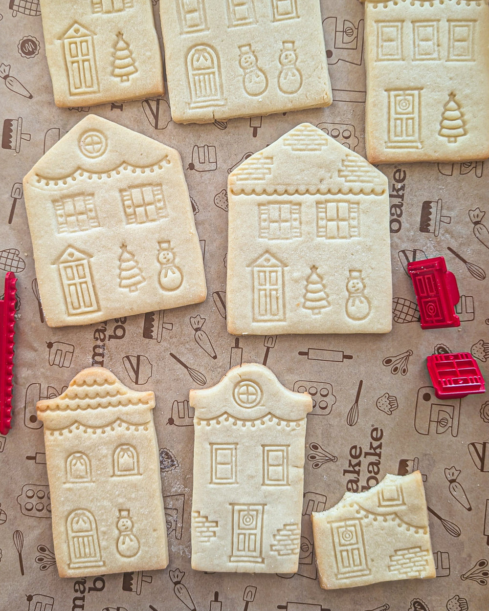 Decorative sugar cookies shaped like houses and stamped with house details on a baking sheet.