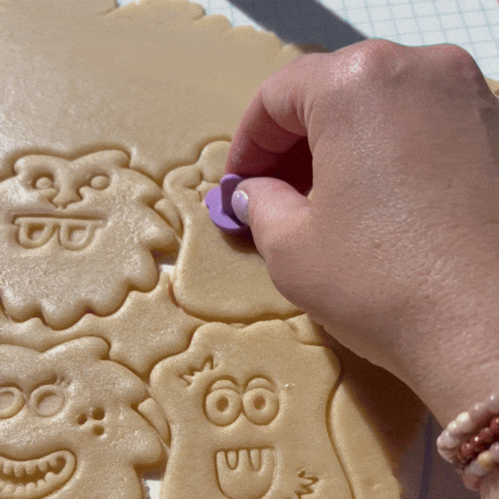Video of a hand stamping monster face parts on sugar cookie dough and the showing them baked.