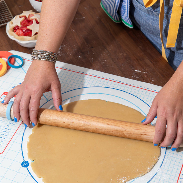 Baker rolling out dough for cookies and pies using a wood rolling pin and adjustable silicone thickness bands
