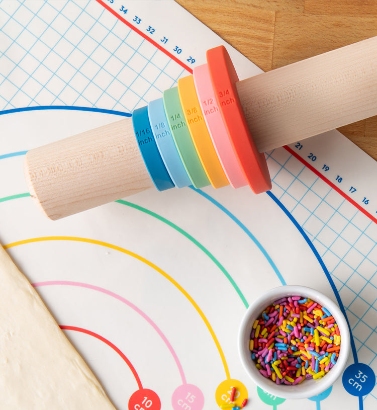 Wooden rolling pin with dishwasher safe adjustable silicone measurement bands in inches and cm on a baking mat with dye-free sprinkles.