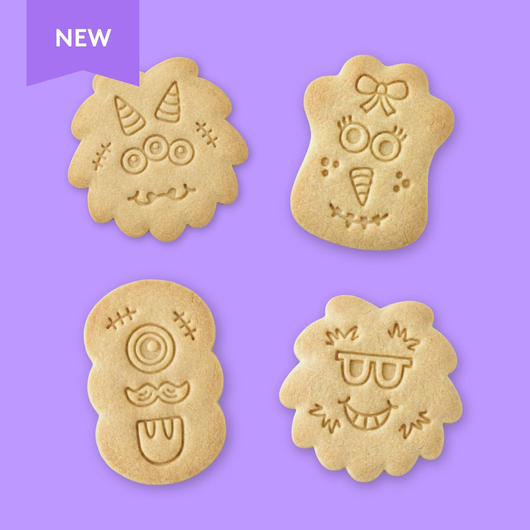 Four monster face-shaped cookies with stamped designs on a red background, labeled 'New Design'.