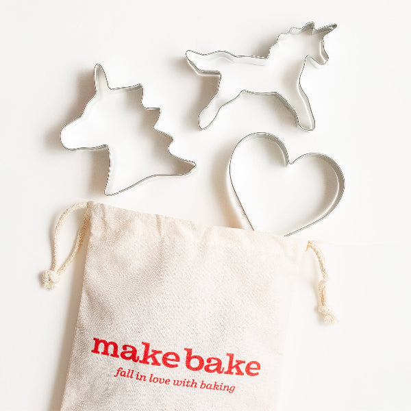 Three cookie cutters shaped like a unicorns and hearts and are styled with a 'make bake' branded drawstring bag for easy storage.