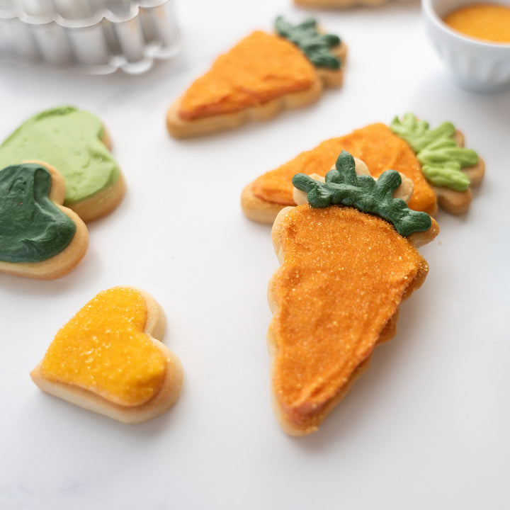 close up carrot and heart cookies in orange and green made with dye free sanding sugars and natural food colors on a white background