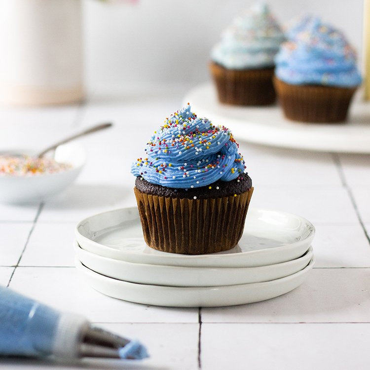 chocolate cupcake with dye free blue frosting and nonpareil sprinkles on a plate