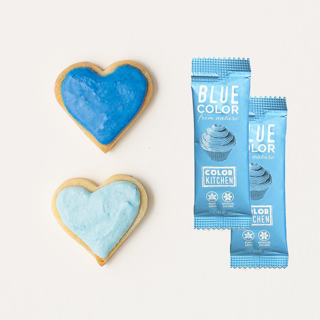 Two packets of blue powdered food color next to heart-shaped cookies decorated with the blue icing.