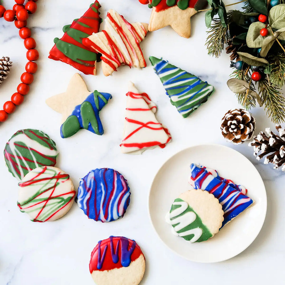 Christmas cookies in a variety of shapes decorated with naturally colored red, blue and green icing on a countertop with mistletoe and pine cones decor