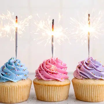 three cupcakes decorated with blue, pink and purple frosting topped with sparklers