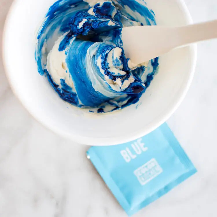 a mixing bowl with dye free blue food color being mixed into frosting