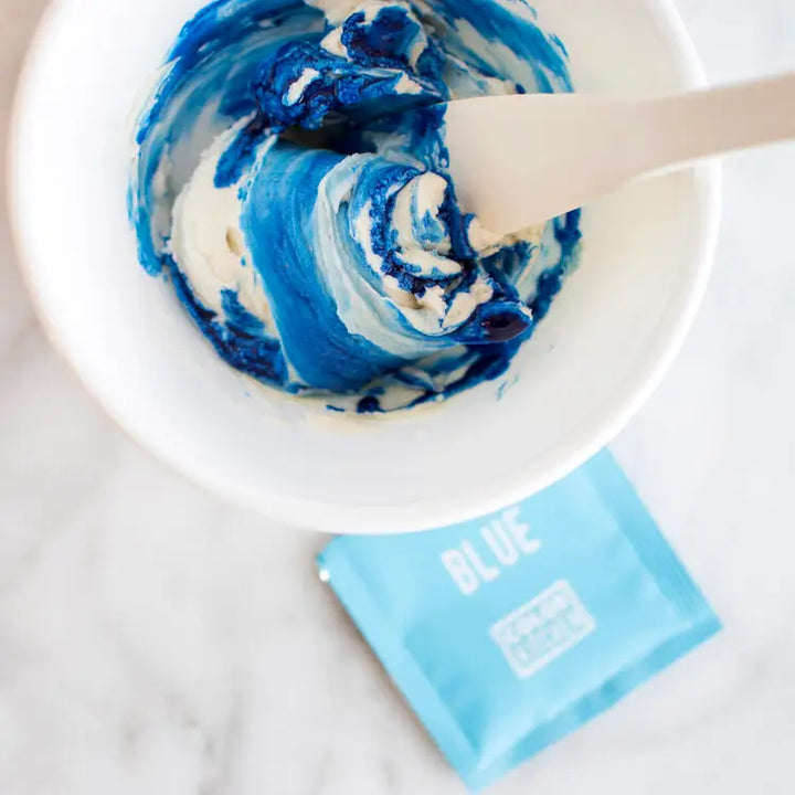 a mixing bowl with dye free blue food color being mixed into frosting