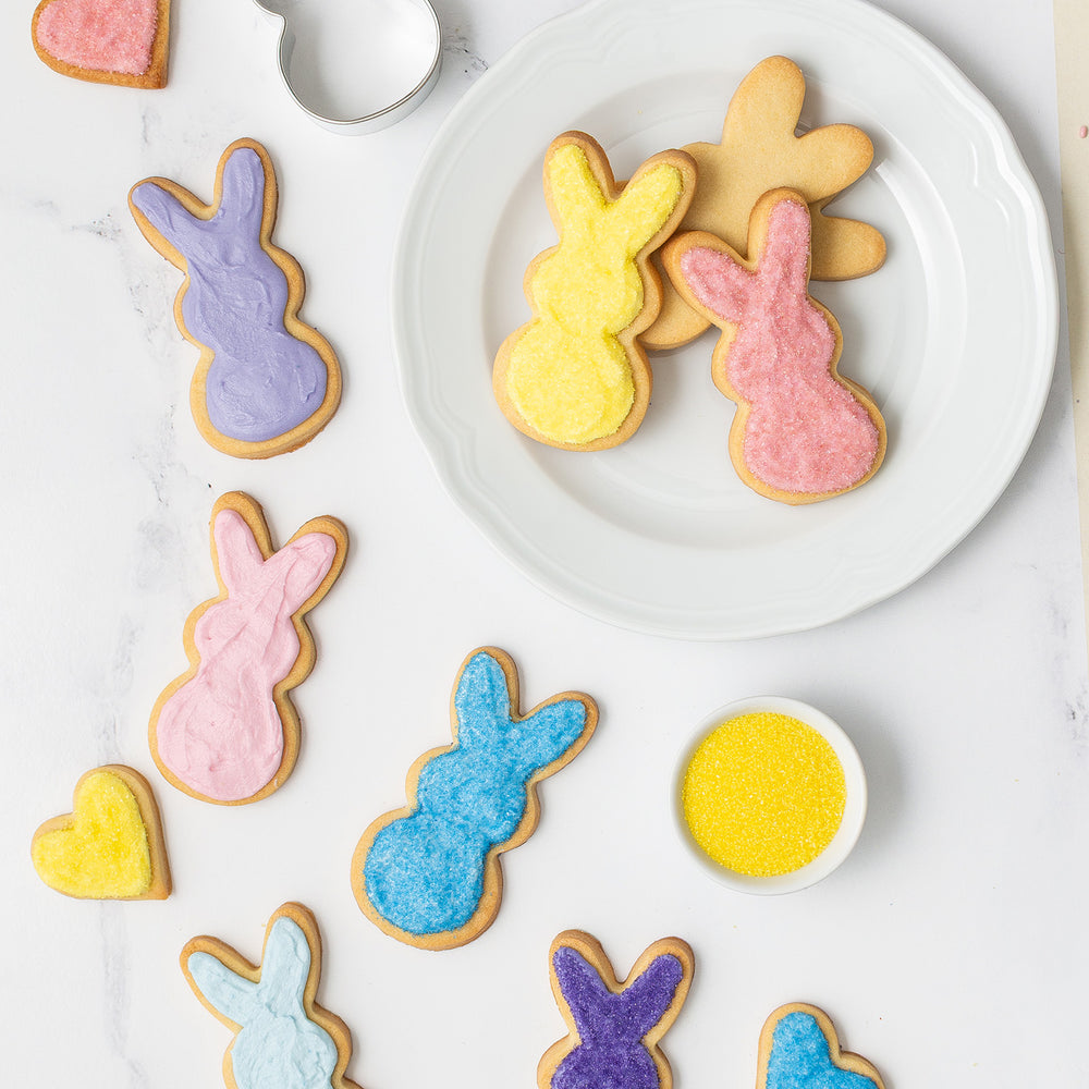 White plate with sugar cookies in bunny shapes decorated with bright and colorful natural frosting and sanding sugars