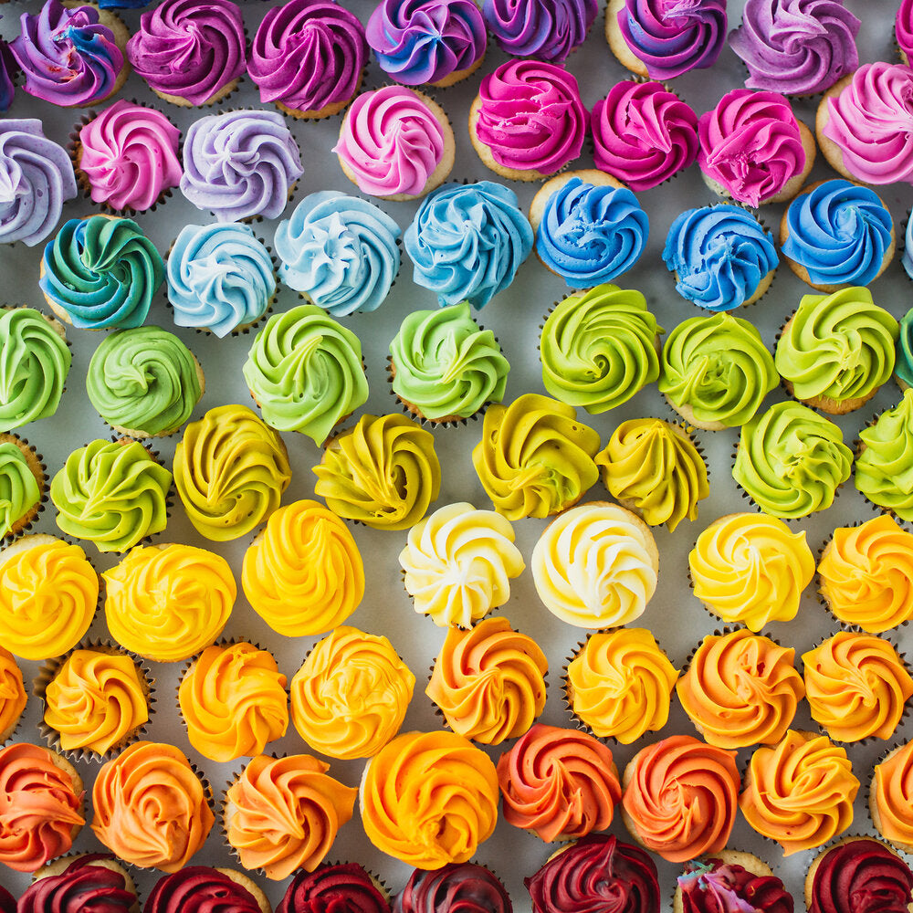 dozens of mini cupcake frosted in rainbow colors using dye free food colors on a white background