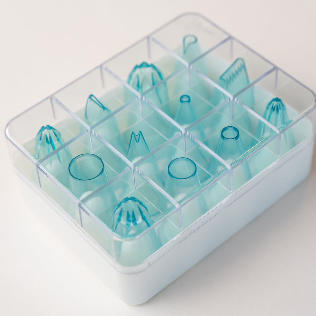 12 pieces clear blue piping tip set in various shapes for cake decorating shown in included plastic storage box.