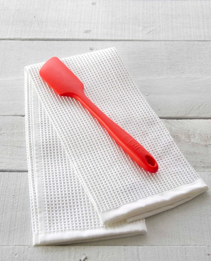 Red spatula on a white textured towel on a light wooden surface