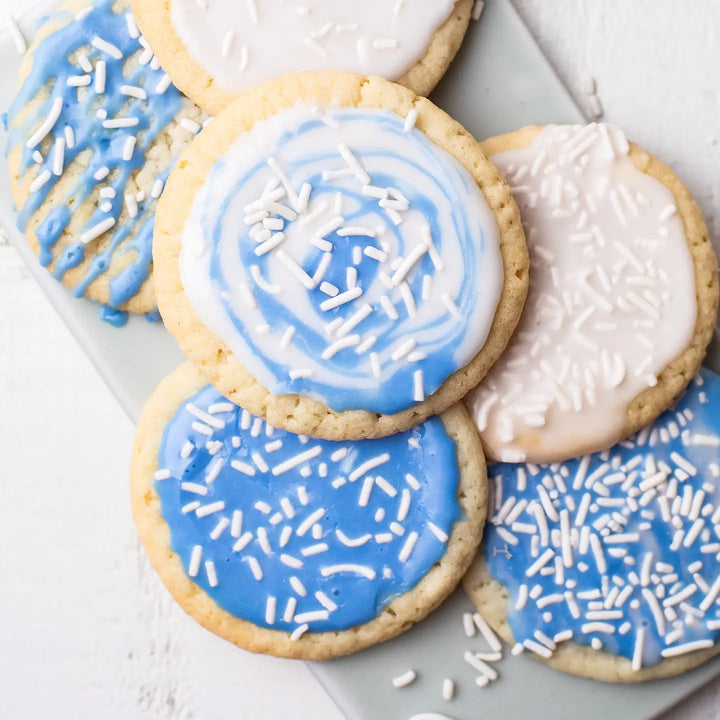 several homemade round sugar cookies covered with blue and white icing and topped with white sprinkles