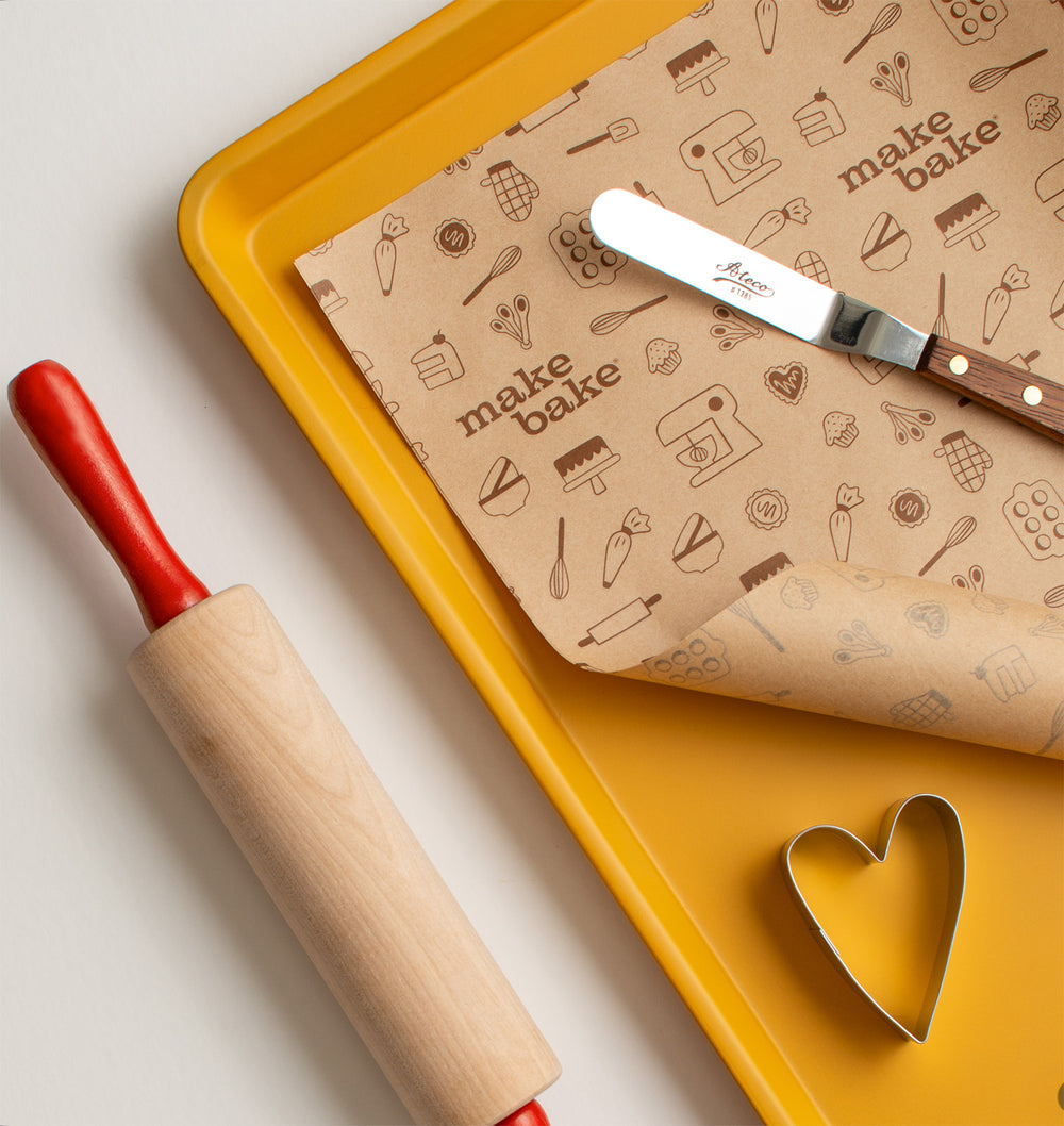 Baking tools including a rolling pin, spatula, and patterned paper on a yellow tray.