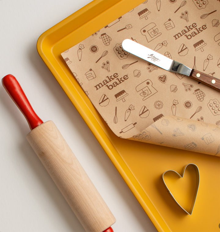 Baking tools including a rolling pin, spatula, and patterned paper on a yellow tray.
