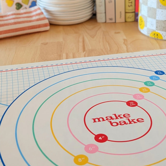 Make Bake Brand Rainbow Roller pastry and dough rolling mat with grid measurement pie measuring circles in rainbow colors shown on a butcher block kitchen countertop.