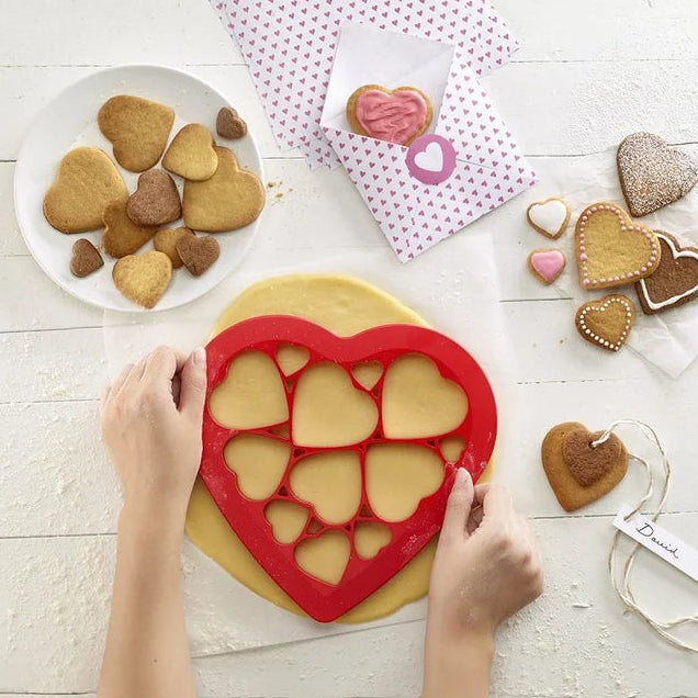 Heart-shaped cookie cutter being used on a cookie dough with heart-shaped cookies and a pink polka dot napkin in the background.