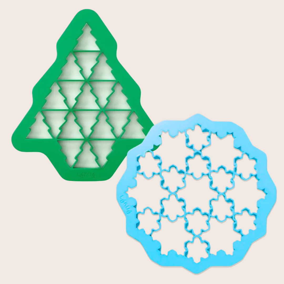 Two plastic cookie cutters on a light beige background: a green tree-shaped cutter and a blue snowflake cutter. Each cutter cuts multiple small cookies at once.