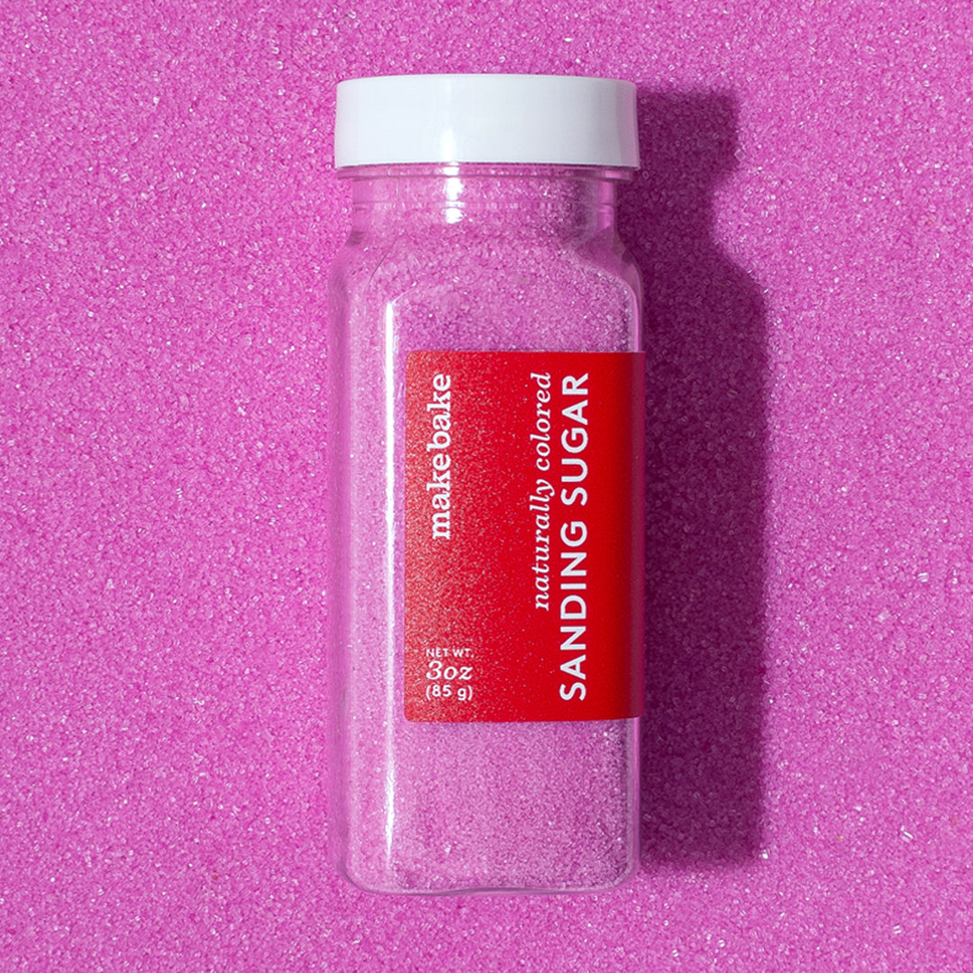 Bottle of Make Bake dye free pink sanding sugar with a red label on a pink sanding sugar background