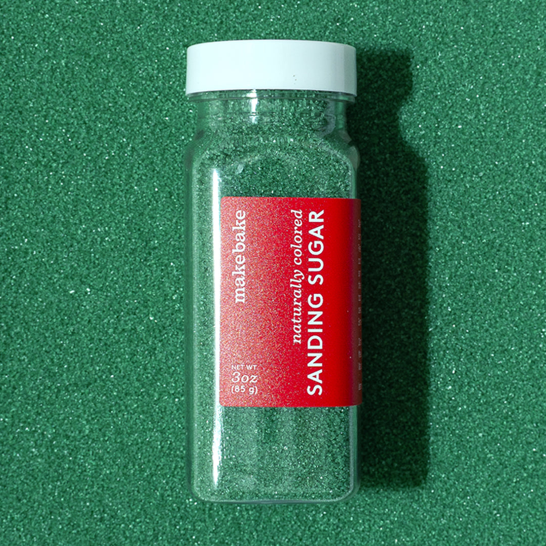 Bottle of Make Bake dye-free green sanding sugar with a red label on a background of naturally colored green sanding sugars