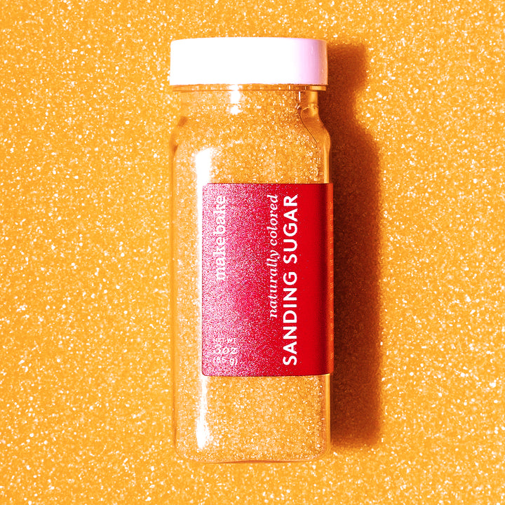 Bottle of Make Bake dye-free orange sanding sugar with a red label that reads "naturally colored sanding sugar 3 ounces"