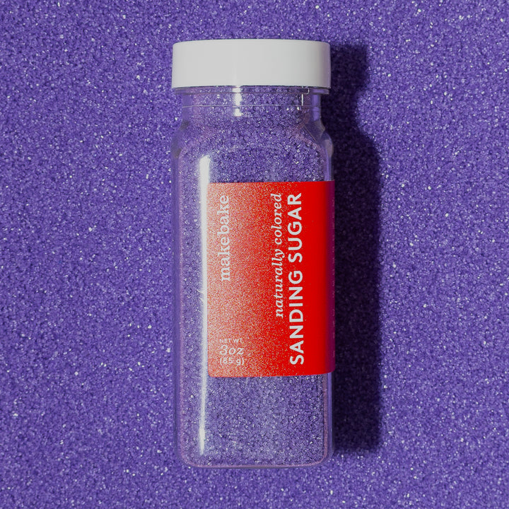 3 oz bottle of Make Bake dye-free purple sanding sugar with a red label on a purple sanding sugar background.