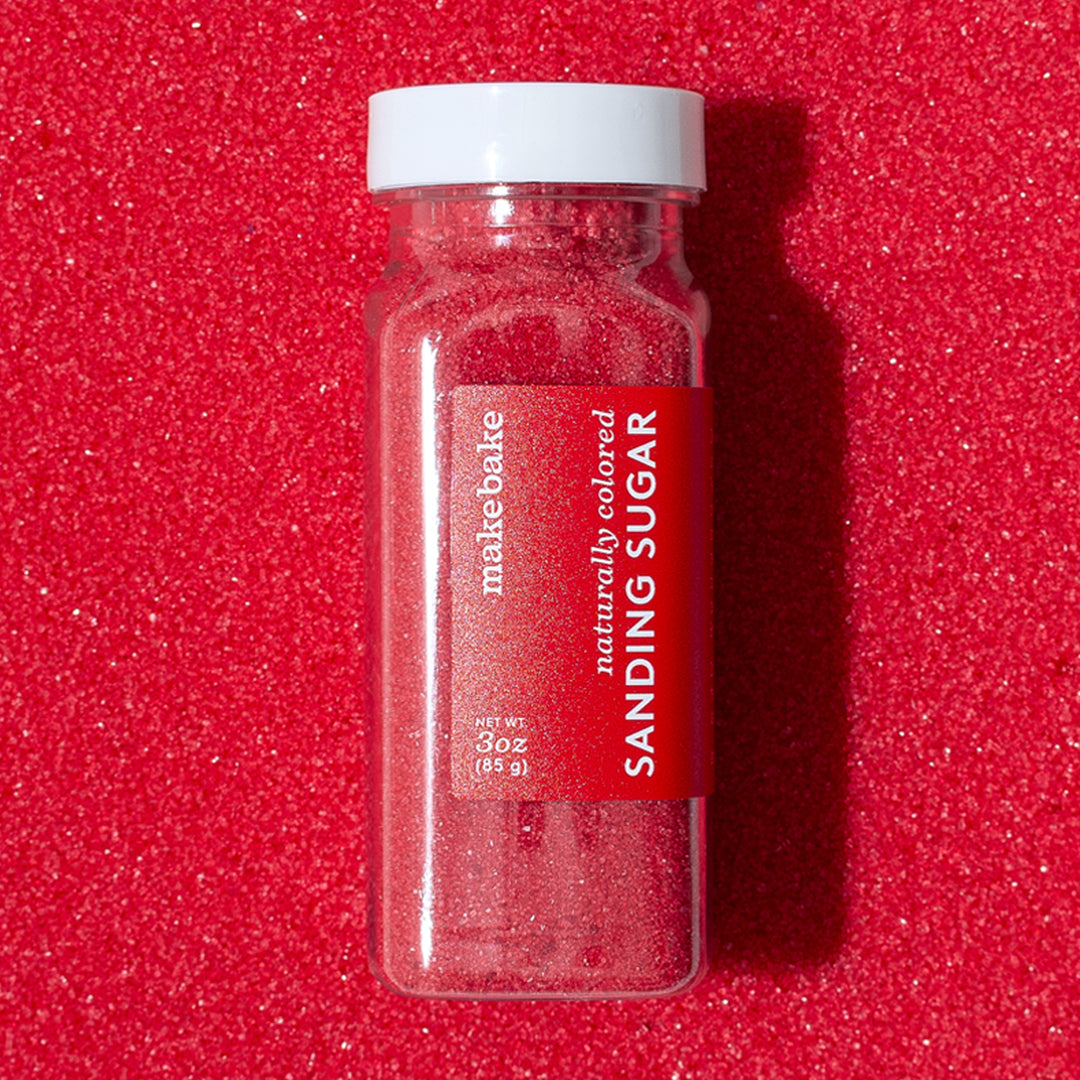 3 oz bottle of Make Bake brand dye-free red sanding sugar with a red label on a background of naturally colored red sugar