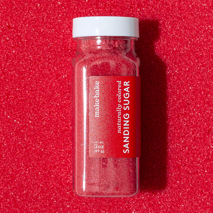 3 oz bottle of Make Bake brand dye-free red sanding sugar with a red label on a background of naturally colored red sugar