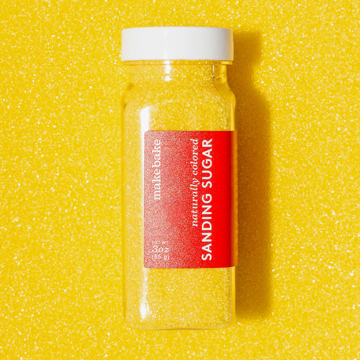 A bottle of Make Bake natural yellow sanding sugar on a background of dye free yellow sugar