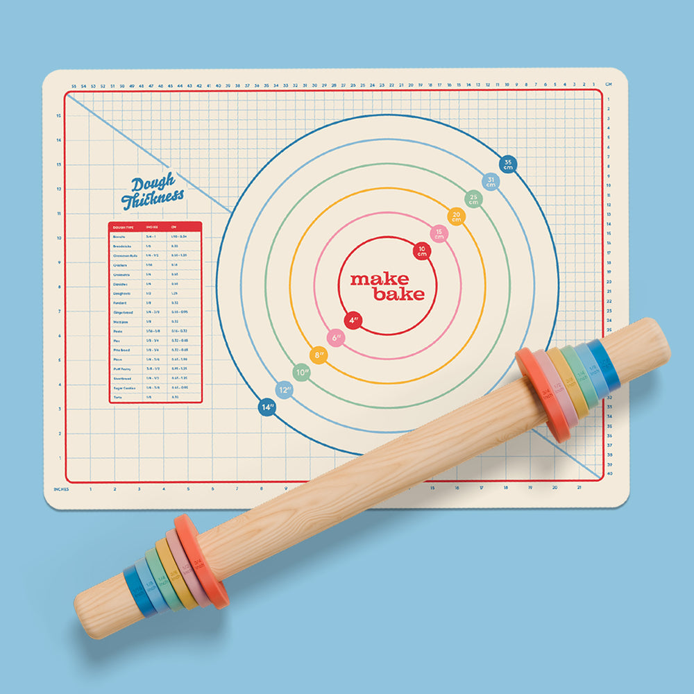 Silicone dough rolling mat with measurements in inches and centimeters with a modern rainbow design and wooden rolling pin with six sets of silicone thickness rings for rolling out dough evenly.