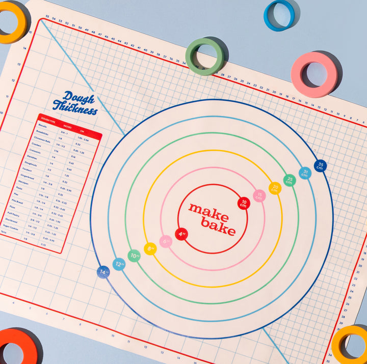 Baking mat with circular measurements and 'make bake' text, surrounded by colorful rings on a blue background.