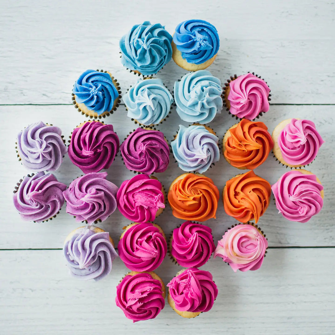 variety of cupcakes decorated with frosting colored with natural food colors in shades of pink, purple, blue and orange