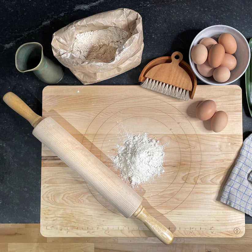 Wooden cutting board with flour, rolling pin, and eggs on a dark surface