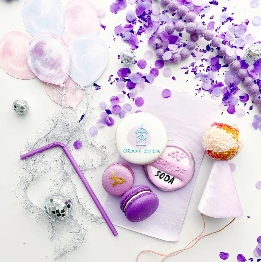 macarons and cookies styled on a table top with purple confetti.