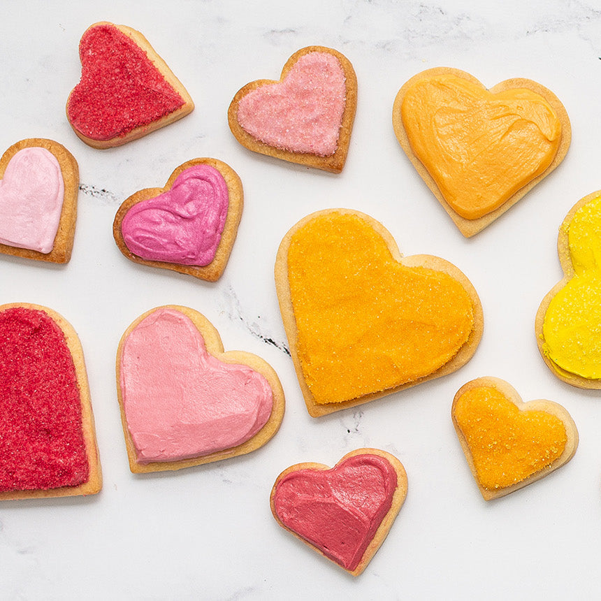 Variety of heart-shaped cookies in various sizes with a variety of dye-free colorful icing on a marble surface.