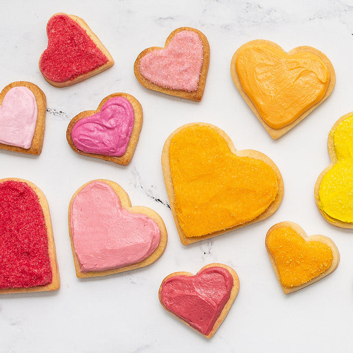 Variety of heart-shaped cookies in various sizes with a variety of dye-free colorful icing on a marble surface.
