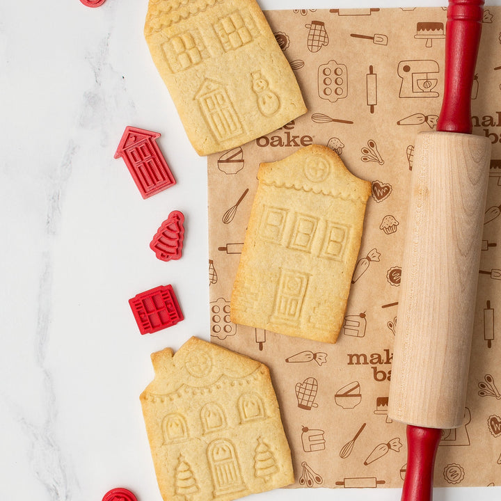 House-shaped cookies with a rolling pin and red cookie cutters on a baking paper.