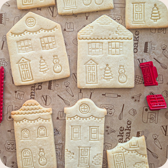 Decorative cookies shaped like houses on a baking paper with kitchen-themed designs.